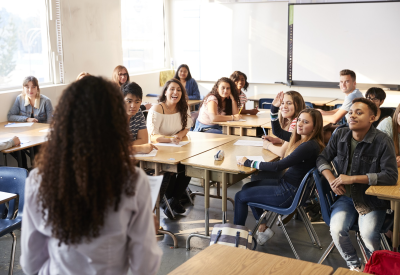 Rear View Of Female High School Teacher Standing At Front Of Class Teaching Lesson