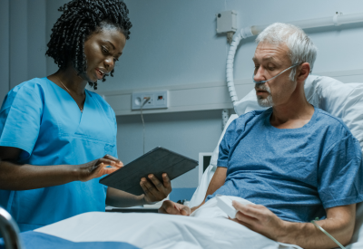 A nurse with a tablet computer talks to an elderly patient in hospital.