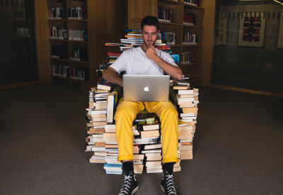 Person sitting in a library on a chair made of books