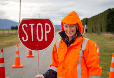A woman on a road crew operates a stop sign at a hazard area on a rural road in Canterbury, New Zealand