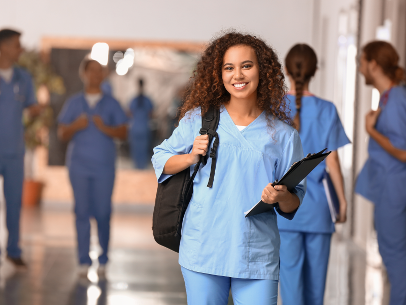 Junge Frau in Medizinal-Arbeitskleidung steht in Korridor und blickt in Kamera