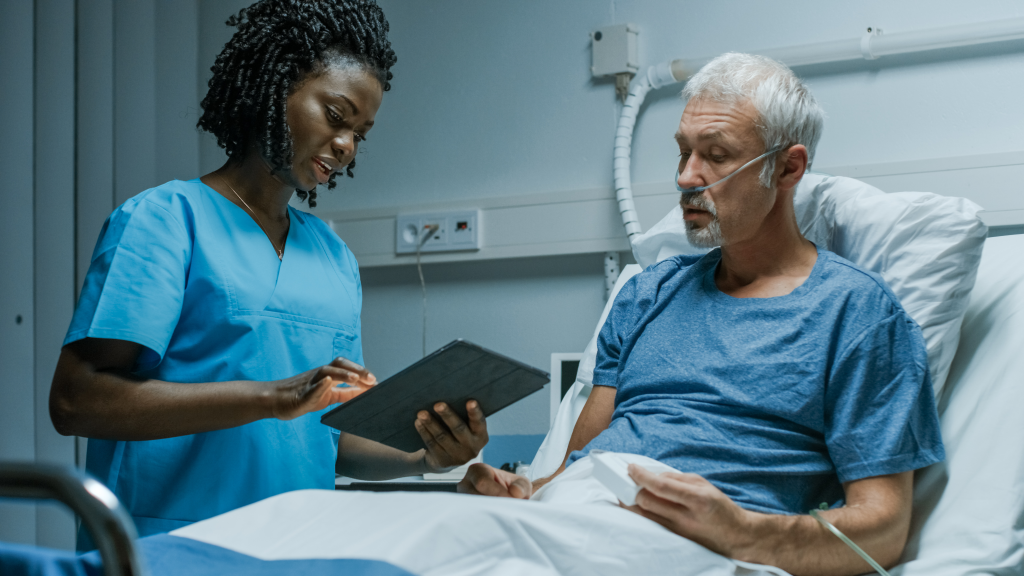 A nurse with a tablet computer talks to an elderly patient in hospital.