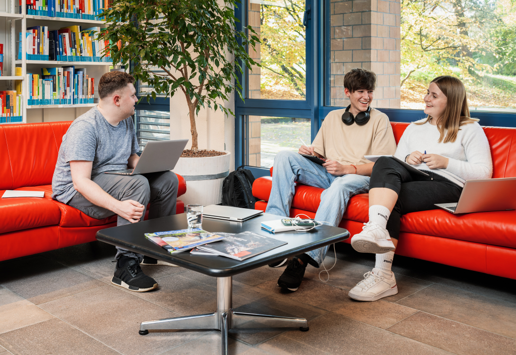 Drei Lernende diskutieren in einer Sitzecke der Bibliothek