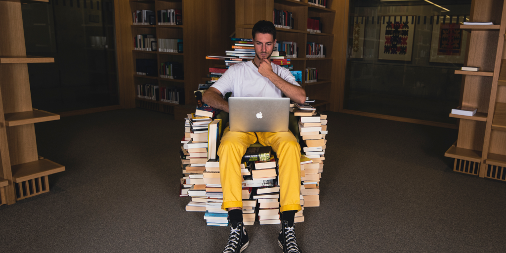 Person sitting in a library on a chair made of books